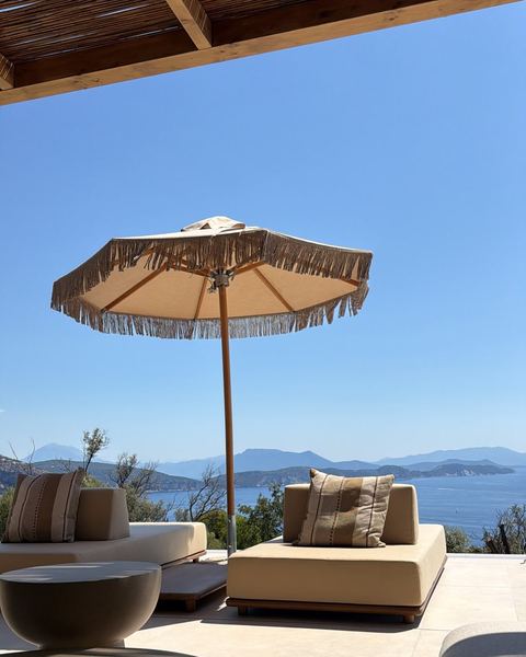 Daybeds with striped cushions under a fringed parasol, overlooking a bay, islands and distant mountains.