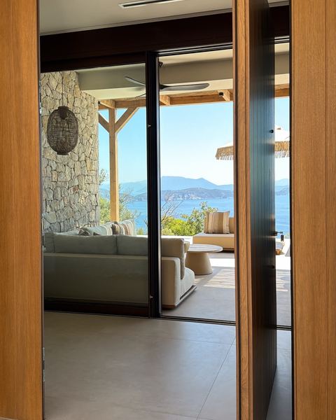 Open timber front door revealing the covered terrace lounge, a woven lantern and the sea beyond.