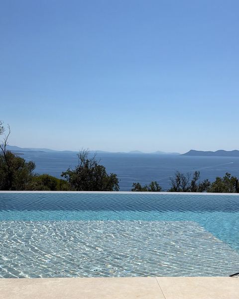 Infinity pool edge merging with the blue sea and hazy islands under a clear sky.