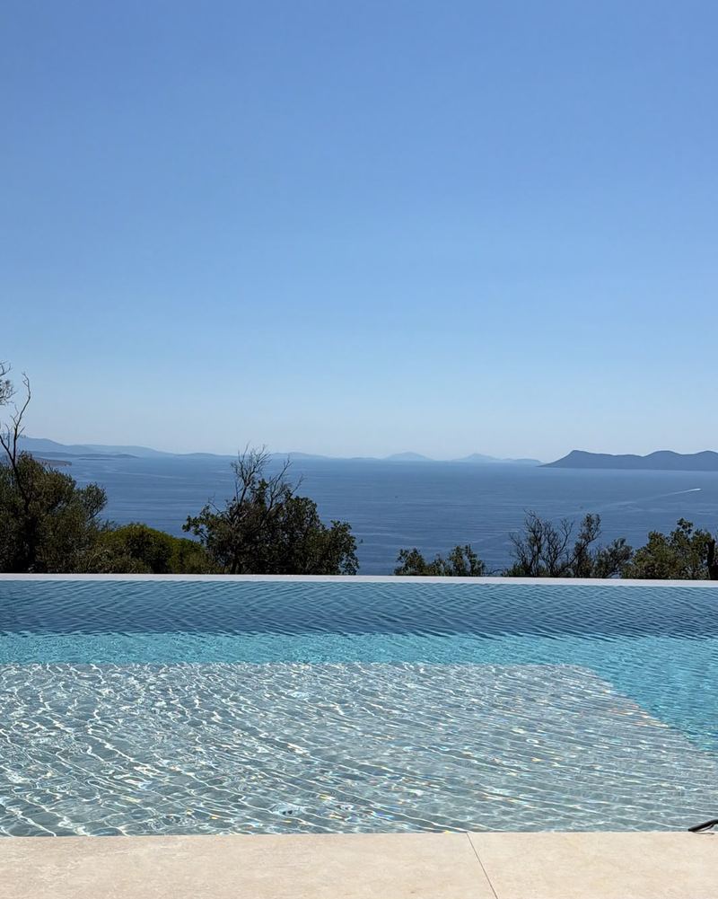 Infinity pool edge merging with the blue sea and hazy islands under a clear sky.