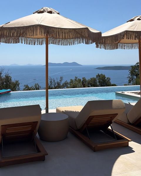 Sun loungers under fringed parasols beside the infinity pool, facing the open sea and distant islands.