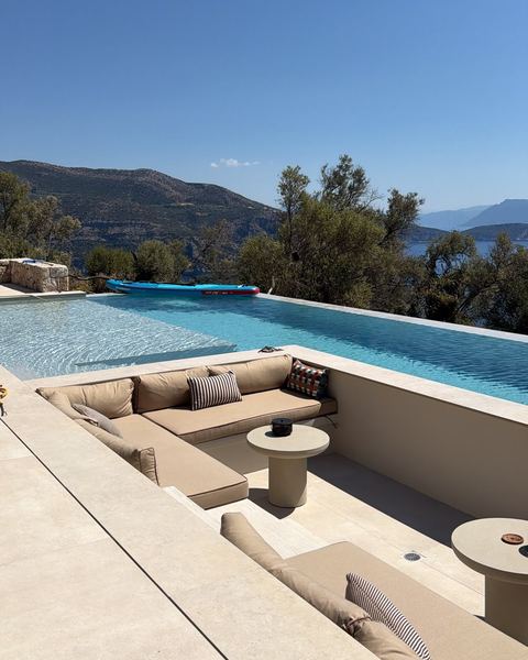 Sunken lounge with cushioned seating set into the infinity pool, overlooking olive trees, hills and the sea.