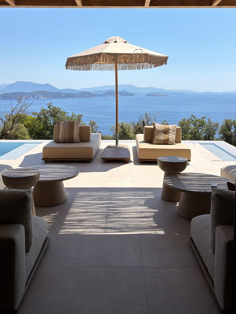 View from the covered terrace across two daybeds and a fringed parasol to the infinity pool, the sea and distant islands.
